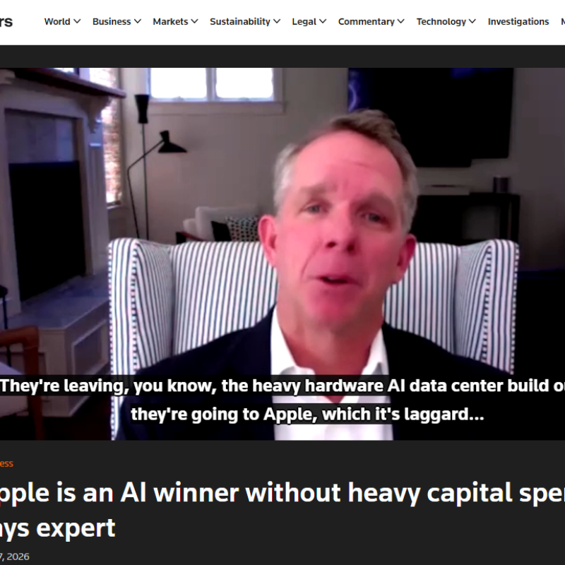 Video interview screenshot of a man in a suit speaking from a striped chair in a home office; onscreen subtitles discuss AI hardware and Apple.